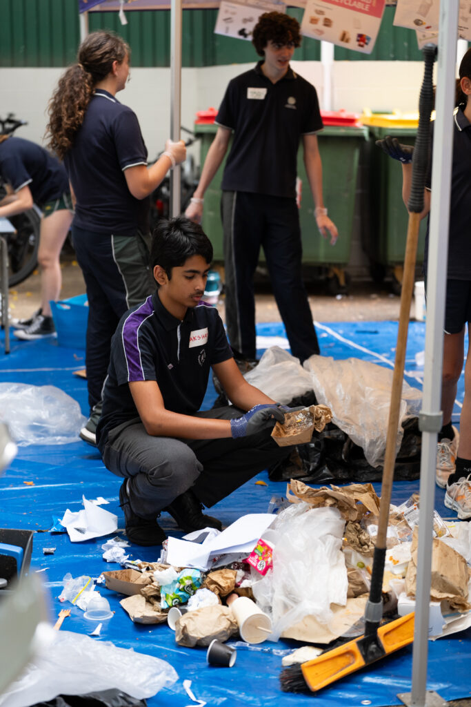 IGS students conduct a Waste Audit indoors, sorting paper and plastic waste on a blue tarpaulin while wearing gloves and uniforms, actively contributing to sustainability initiatives ahead of 2026.