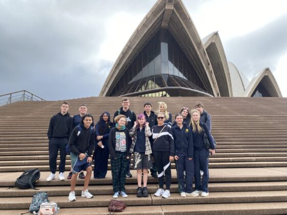 A group of students pose together on the steps of the Sydney Opera House, with its iconic sails visible in the background under a cloudy sky, celebrating their achievements in Aboriginal Studies.