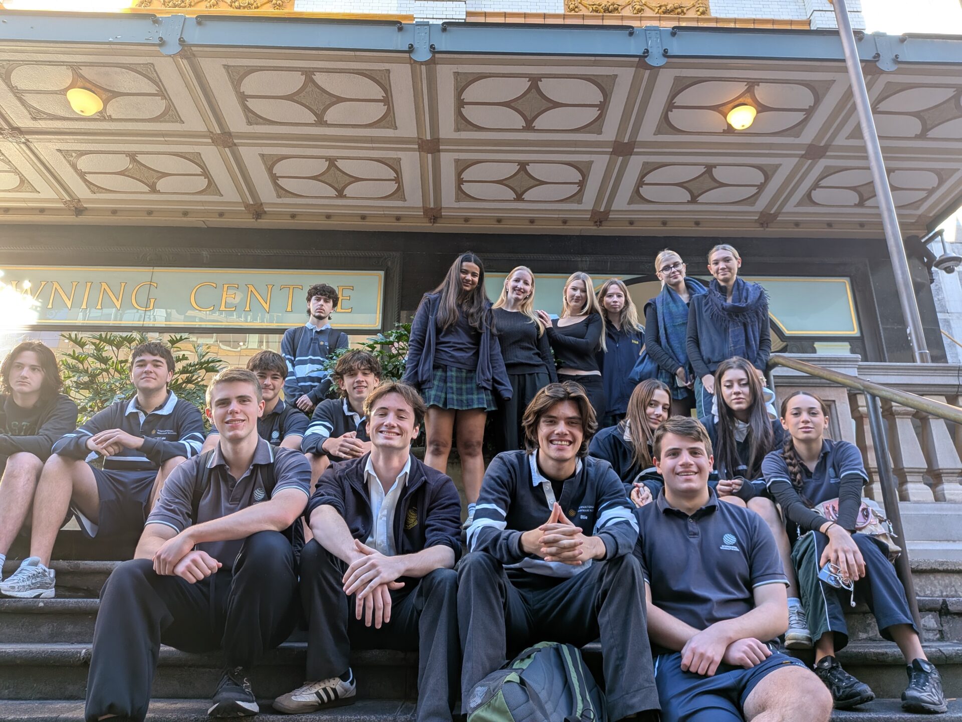 A group of students in school uniforms sit and stand on steps outside a building with a sign that reads LEARNING CENTRE. Smiling and posing for a group photo, they look ready to explore the legal world.