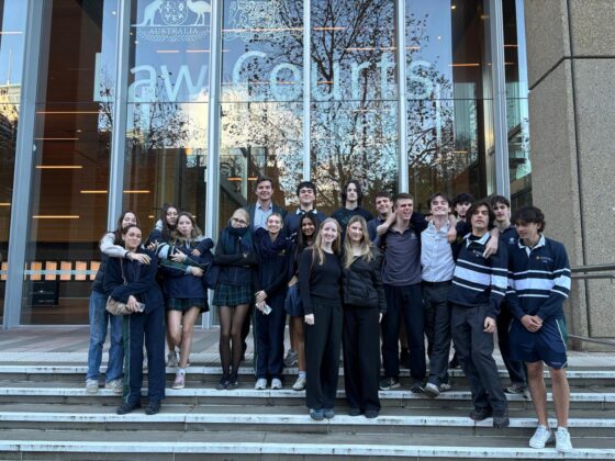 A group of young people stands and poses for a photo on the steps in front of a modern courthouse building, ready to embark on their journey into the legal world, with large glass windows and law courts written above the entrance.