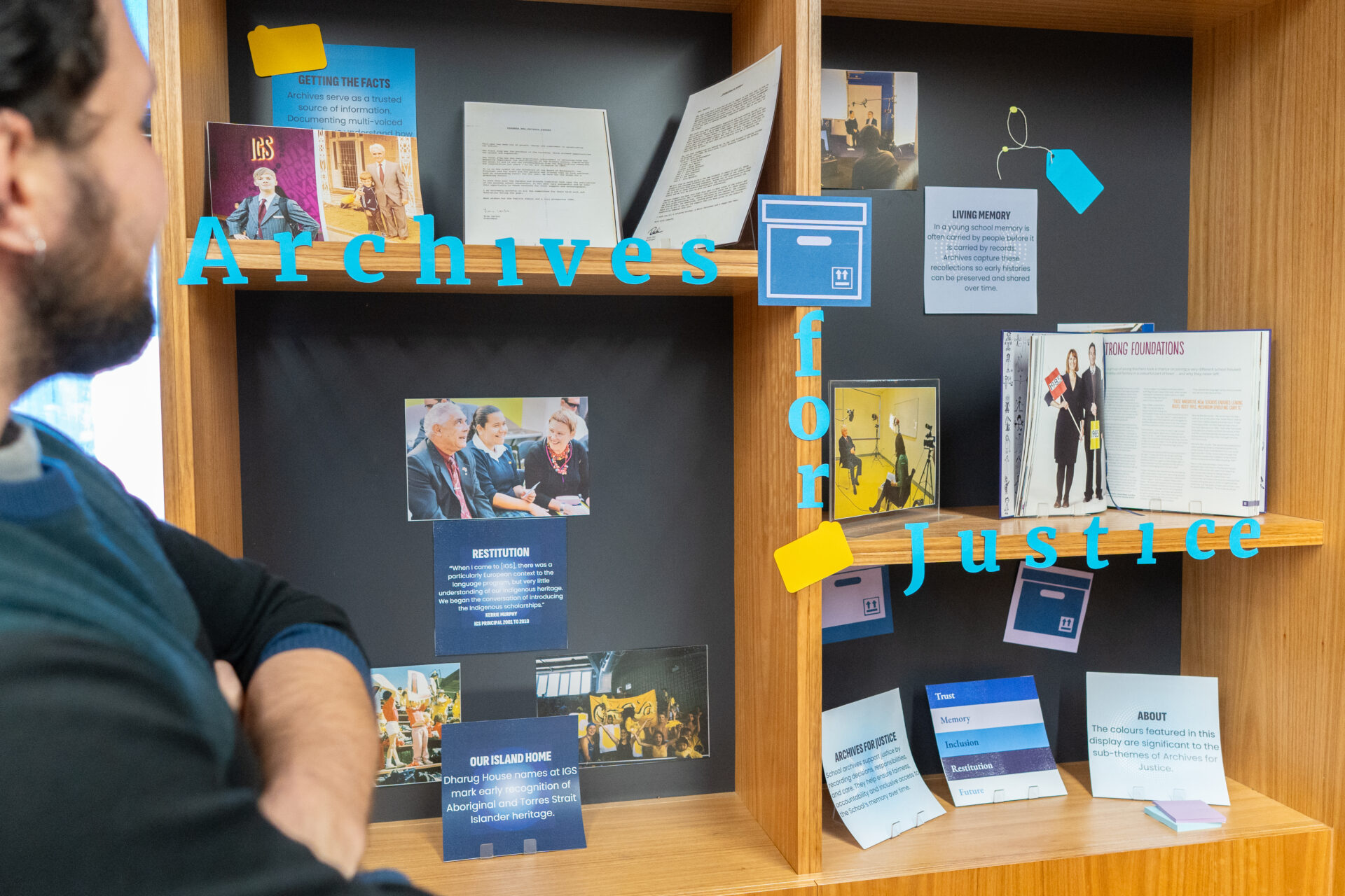 A person stands in front of a wooden display case filled with documents, photos, and cards under the words “Archives for Justice” in blue text across the glass, highlighting Archives in Action.
