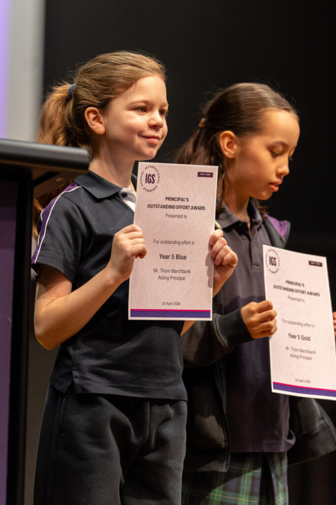 Two young girls in school uniforms stand side by side, each holding a certificate for the Headteacher’s Outstanding Effort Award, recognising their term sports achievements. The certificates feature the school’s logo and details.