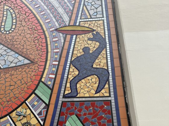 Mosaic art showing a blue silhouette of a person reaching up towards a yellow oval shape, bordered by colourful geometric patterns—a vibrant tribute inspired by Hidden Figures.