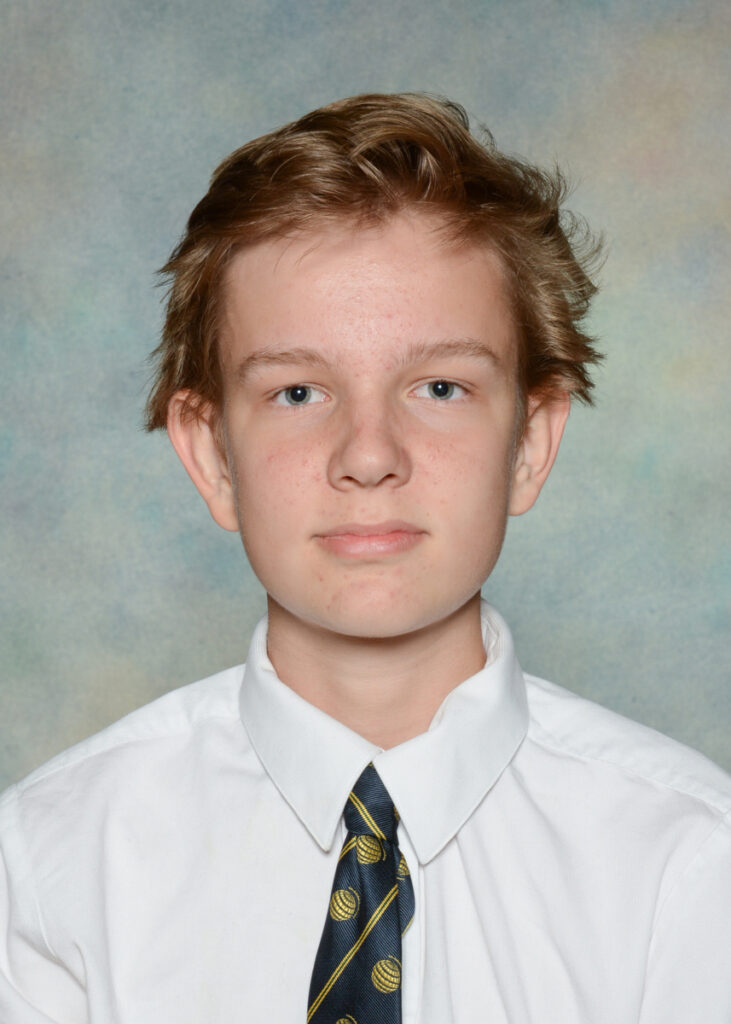 Teen boy with short light brown hair, wearing a white dress shirt and patterned tie, poses for a school portrait in front of a neutral, softly coloured background—a timeless look reminiscent of an episode 38 “Triple Play” moment from WITWAT.