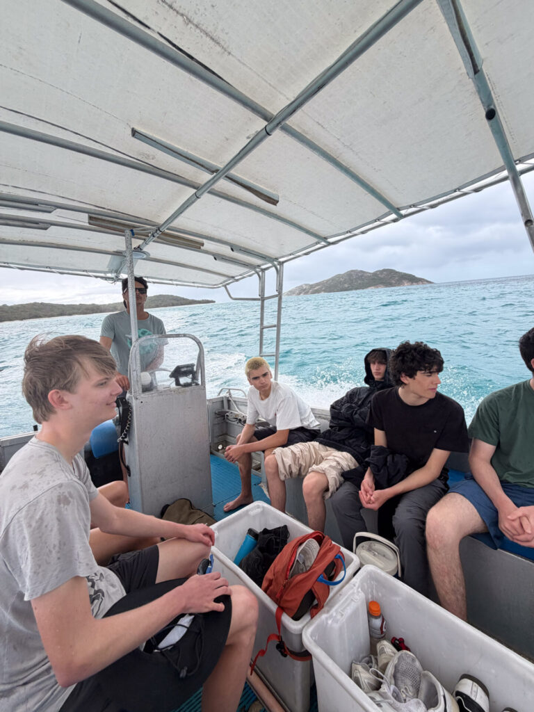A group of young men travelling on a small boat across choppy water.