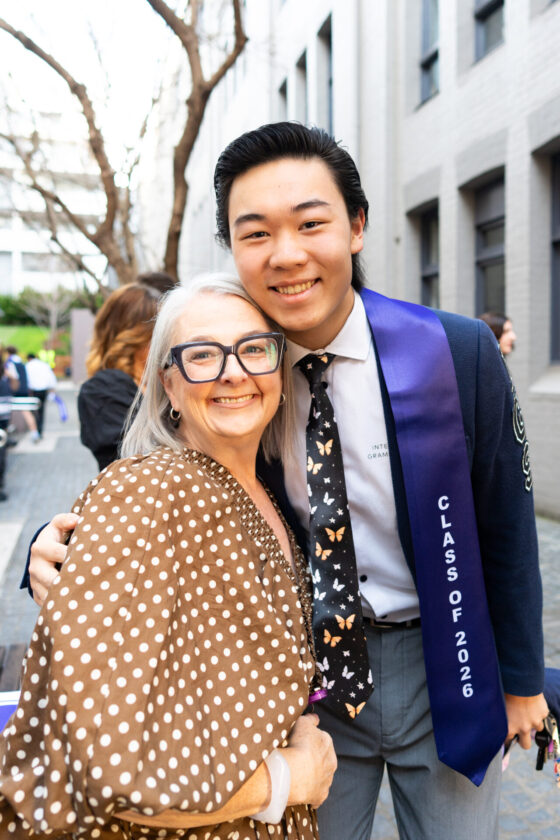 A young man in a graduation sash labelled Class of 2026 hugs an older woman.